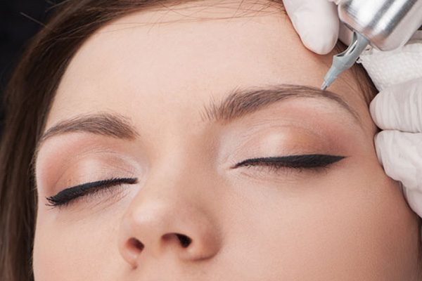 beautiful young lady getting tattoo. professional tattooist making eyebrow make up